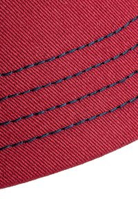 Tissu rouge avec une finition texturée, comportant trois lignes parallèles de couture bleue. Le matériau semble durable et étroitement tissé.