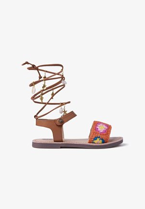 Sandalo in pelle marrone con cinturino intrecciato multicolore a motivo floreale. Presenta un laccio a spirale con ciondoli decorativi, che conferisce un elemento di design unico.