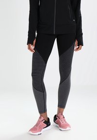 Czarno-szare legginsy sportowe z geometrycznym wzorem, pasami i elastycznym materiałem, w zestawieniu z różowymi butami sportowymi.