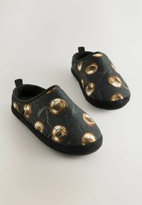 Pár čiernych šľapiek na slip-on so zlatými potlačami futbalových lôpt a čiernymi podrážkami na svetlom pozadí.