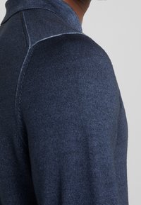 Marineblaues Strickpullover mit strukturiertem Stoff, einem Kragen und figurschmeichelndem Design. Nahtdetails sind an den Schultern sichtbar.