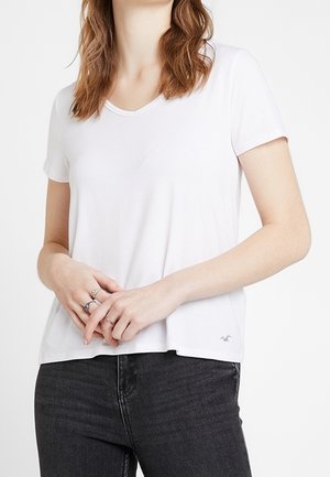 Biała koszulka z krótkim rękawem i dekoltem w serek, wykonana z lekkiego materiału. Posiada małe logo u dołu po lewej stronie oraz luźny krój.