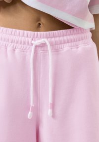 Roze katoenen sweatpants met een elastische tailleband, voorzien van een witte trekkoord en een gestructureerde stof. Geen zichtbare patronen of accenten.