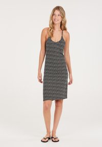 Vestido de estampado en blanco y negro con tirantes finos tipo spaghetti, corte hasta la rodilla y silueta ajustada. Combinado con sandalias planas negras.