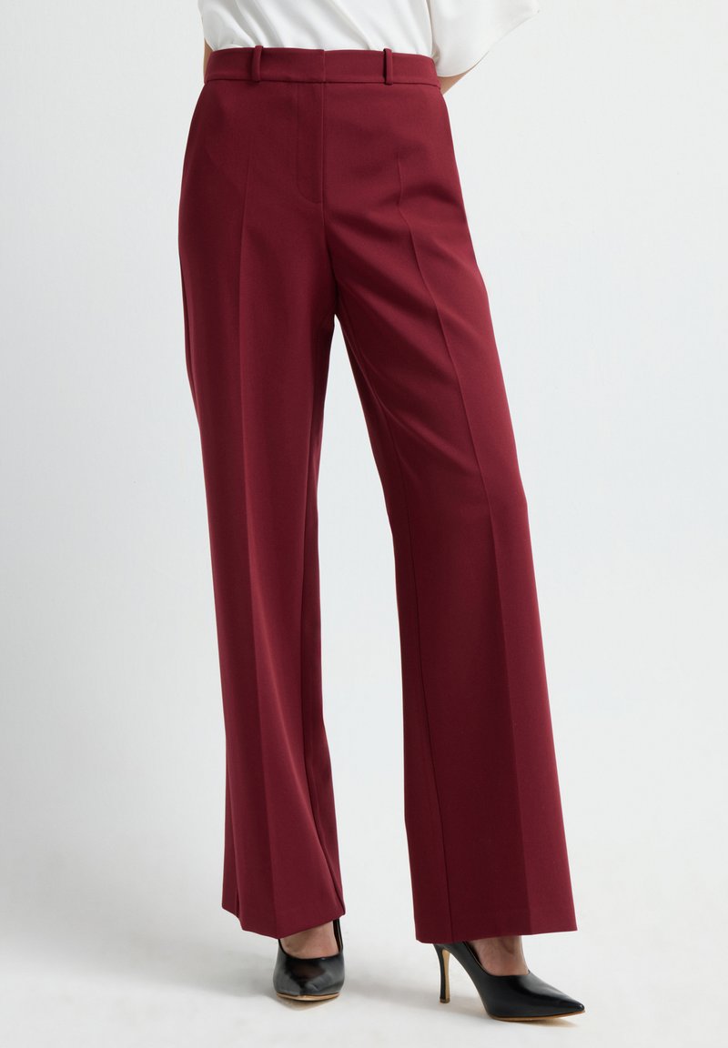Burgundy wide-leg trousers with a smooth texture, high waistband, and front pleats, paired with black high-heeled shoes.