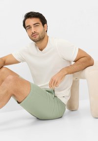 T-shirt corta beige chiaro abbinata a pantaloni corti verde menta. I pantaloni corti hanno tasche laterali e una texture liscia e opaca. Design minimalista.