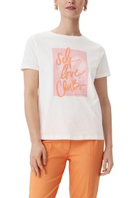Weißes Baumwoll-T-Shirt mit einem pinken Grafikdesign und dem Text "Self Love Club". Kurze Ärmel und eine lockere Passform, kombiniert mit orangenen Hosen.