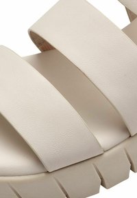 Sandale à plateforme beige clair avec trois larges brides en matériau texturé, dotée d'une semelle épaisse et nervurée pour une meilleure adhérence et un bon soutien.