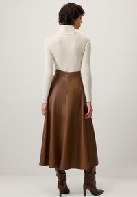 Rjava usnjena midi krilo z gladko teksturo in subtilnim sijajem, združena s oprijeto kremasto polo puloverjem. Čevlji so do kolen v temno rjavi barvi.