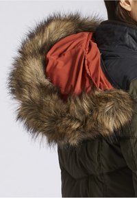 Parka-jakke med en aftagelig hætte, der har en brun faux fur-beklædning og en indvendig orange foring. Udsiden er mørkegrøn med kviltet tekstur.