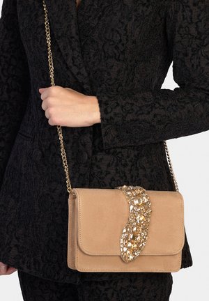 Beige Wildleder-Umhängetasche mit dekorativem goldakzentuiertem Verschluss, ausgestattet mit einer Kettenriemen und einem klaren, strukturierten Design.