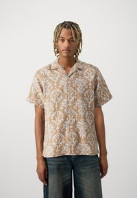Camicia a maniche corte con bottoni in beige e bianco con un motivo floreale vorticoso, realizzata in tessuto leggero; vestibilità ampia e design del colletto.