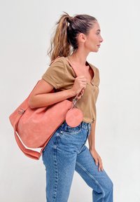 Femme avec une queue de cheval portant un haut beige et un jean bleu, portant un grand sac à bandoulière rose avec un porte-monnaie rond attaché.