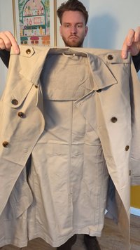 Trench coat bege com grandes botões castanhos, design de duplo botão e uma silhueta estruturada. Textura suave com colarinho e bolsos.