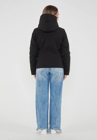 Giacca isolante nera con cappuccio, design aderente e maniche lunghe. Indossata con jeans a gamba larga blu chiaro e sneakers bianche.