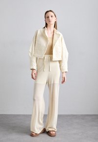 Veste texturée raccourcie et pantalon en tricot léger, ample, de couleur crème. L'ensemble présente une coupe décontractée et une taille élastique avec cordon de serrage. Sandales plates.