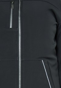 Černá zipová bunda vyrobená z hladkého, pružného materiálu, která má přední zip, kapsu na levé hrudi a bílé lemování na kapsách.