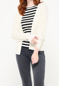 Lätt, krämfärgad, fluffig kardiagan med öppen front, långa ärmar och en mjuk textur, tillsammans med en topp med svart och vit rand.