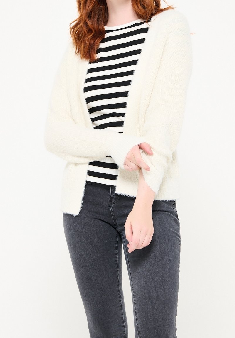Lätt, krämfärgad, fluffig kardiagan med öppen front, långa ärmar och en mjuk textur, tillsammans med en topp med svart och vit rand.