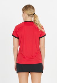 Punainen urheilusinta mustilla yksityiskohdilla, lyhyet hihat ja pyöreä pääntie, yhdistetty mustan hameen kanssa. Sileä rakenne, istuva muotoilu.