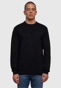 Schwarzer langärmeliger Pullover aus einem weichen Strickstoff mit Rundhalsausschnitt und gerippten Bündchen, getragen über blauen Jeans.
