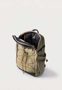 Λαδί πράσινο σακίδιο με μαύρες και κίτρινες λεπτομέρειες από κορδόνι, μερικώς ανοιχτό φερμουάρ στην κορυφή που αποκαλύπτει το μαύρο εσωτερικό και το λογότυπο K-Way στο εσωτερικό.