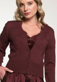 Bordeaux gestrickte Cardigan mit Herz-Ausschnitten und schwarzen Strass-Akzenten. Mit geripptem Saum und fünf-Knopf-Verschluss. Weicher Stoff.