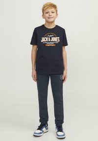 Camisa de algodón azul marino con texto gráfico en blanco y naranja, combinada con pantalones de chándal azul oscuro y zapatillas blancas con acentos azules.