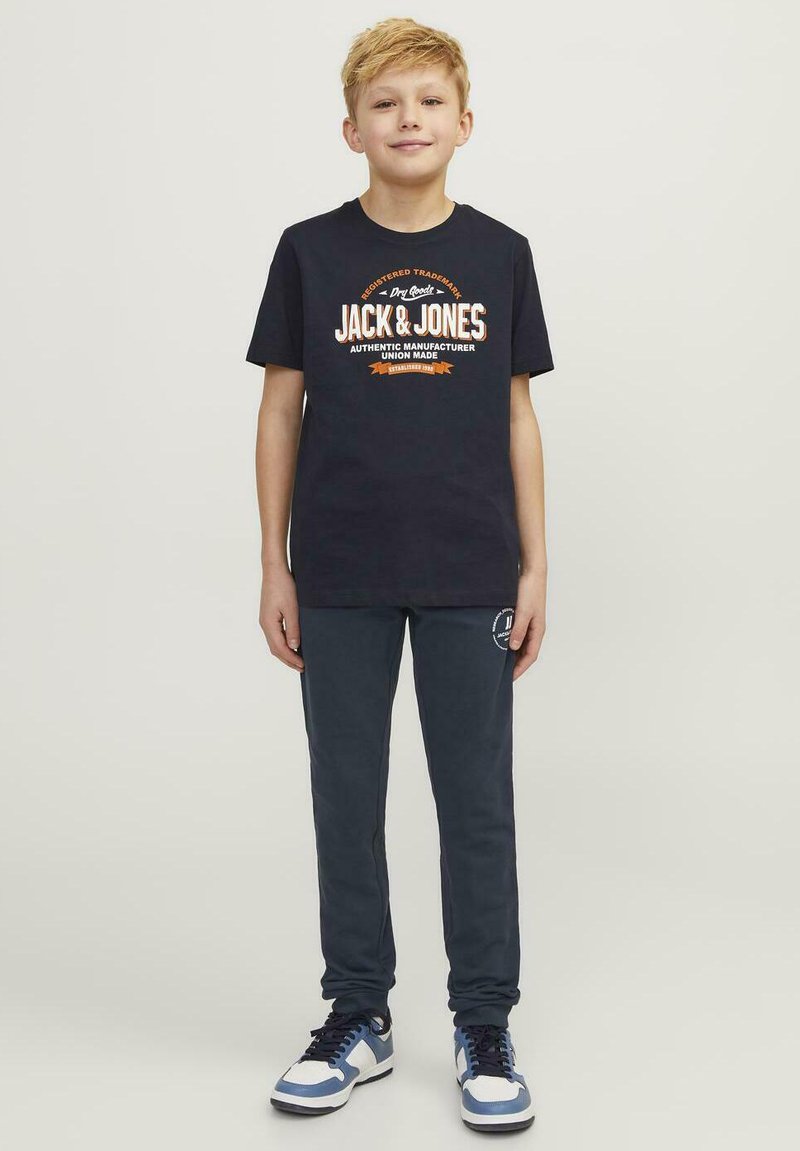 Camisa de algodón azul marino con texto gráfico en blanco y naranja, combinada con pantalones de chándal azul oscuro y zapatillas blancas con acentos azules.