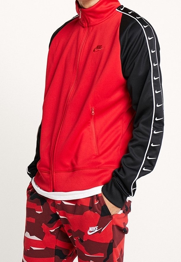 Červeno-černá bunda na zip z hladké látky s vysokým límcem, kapsami na zip a logem. Ozdobena bílými pruhy a značkováním.