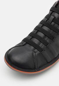 Scarpa in pelle nera con punta arrotondata, caratterizzata da dettagli in pizzo intrecciato, una parte superiore testurizzata e un accento arancione sulla suola.