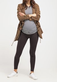 Conjunto de maternidad que presenta una chaqueta caqui sobre una camiseta de rayas blanca y negra y leggings negros, completado con zapatillas blancas.