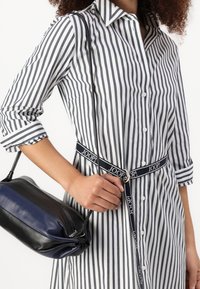 Pruhovaná košilová šaty v bílé a námořnické modři, zapínané na knoflíky s límečkem. Obsahuje černou a námořnickou tašku, drženo po straně odpovídajícím popruhem.