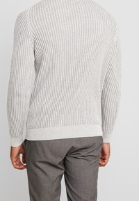 Helles graues, geripptes Sweatshirt mit langen Ärmeln, strukturierter Stoff und Rundhalsausschnitt, kombiniert mit grauen Anzughosen, von hinten gesehen.