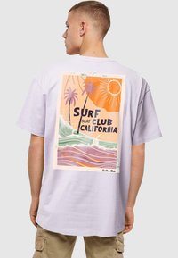 Valkoinen laventelinvärinen puuvillapaita, jossa on selässä grafiikka palmupuista, aalloista ja auringosta oranssin, vihreän ja sinisen sävyissä, teksti "Surf Club California."