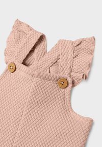 Romper leggero di colore rosa chiaro con spalline arricciate, caratterizzato da due bottoni di legno rotondi per la chiusura su un tessuto con un motivo sottile.