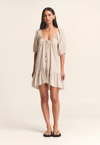 Vestito in tessuto leggero a righe con scollatura rotonda, maniche a sbuffo e orlo a balze sovrapposte. Accentuato da un fiocco e da perline in legno naturale.