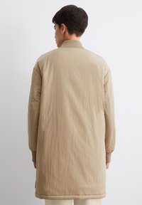 Khaki lange jas met een geribbelde kraag, textuurstof en lange mouwen, met een rechte snit en subtiele stikdetails.