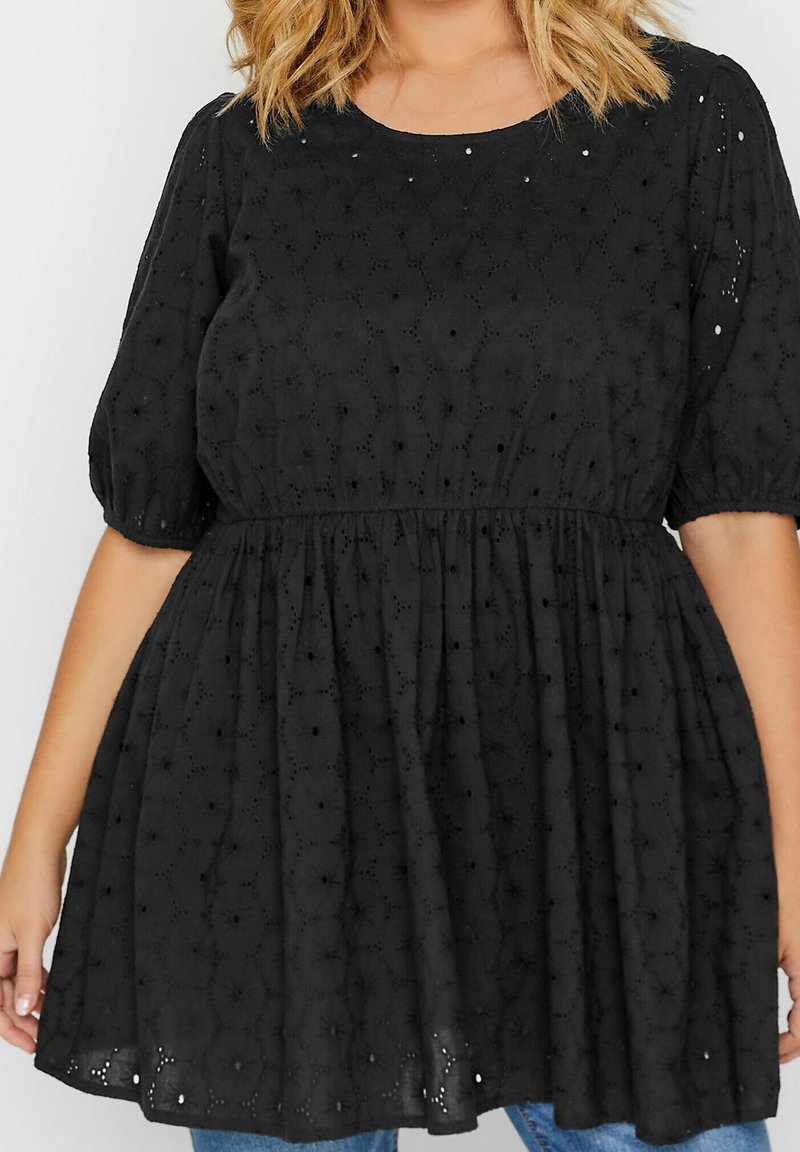 Robe noire à manches courtes présentant un tissu texturé avec des détails en œillets, une taille cintrée et une jupe évasée. Encolure ronde et coupe ample.