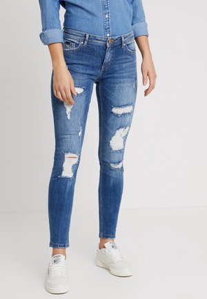 Jeans ajustados de mezclilla azul con detalles desgastados, que presentan múltiples patrones de rasgaduras en las piernas y un diseño estándar de cinco bolsillos.