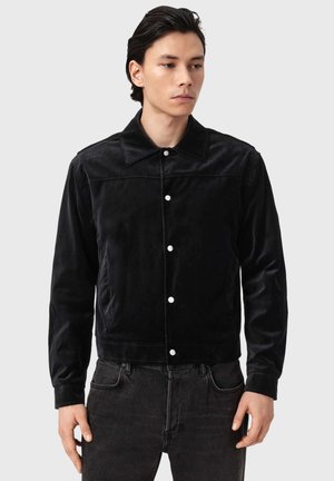 Sort kordjakke med krave, frontknapper og sidelommer. Glat tekstur med en let figursyet silhuet.