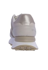 Zapatillas ligeras de cuero beige con acentos metálicos, suela acolchada y detalle trasero texturizado. Presentan un acabado suave y suela texturizada.
