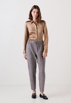 Satin-braune Bluse mit Kragen, kombiniert mit grauen gemusterten Hosen mit elastischem Bund und schwarzen Loafern mit Kettenakzent.