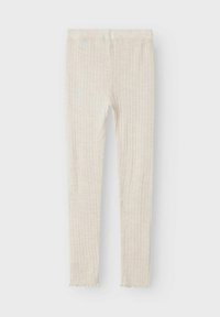 Leggings côtelés beige clair avec un motif texturé, offrant une coupe ajustée et un ourlet décoratif en forme de scallop au niveau des chevilles.