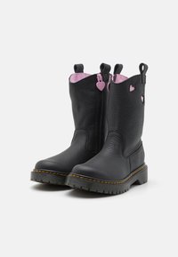 Stivali alla caviglia in pelle nera con interno rosa, cerniera laterale con un tirante a forma di cuore e cuciture gialle a contrasto su una suola robusta.