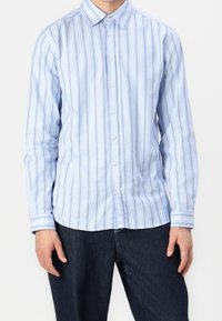 Jasnoniebieska, długorękawowa koszula zapinana na guziki z pionowymi paskami w ciemniejszym niebieskim i beżowym kolorze. Posiada klasyczny kołnierzyk oraz mankiety zapinane na guziki.