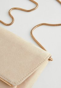 Pochette en suédine beige avec une chaîne en métal doré, dotée d'une fermeture à rabat et de coutures le long des bords.