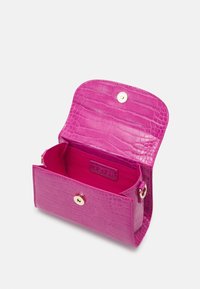 Różowy portfel ze skóry z wzorem krokodyla, zapinany na magnes; posiada otwarte wnętrze oraz naszywkę z logo wewnątrz.
