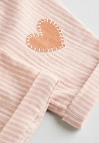 Tela de rayas rosas con un parche de corazón de cuero cosido. El material es suave y texturizado, con rayas horizontales en tonos de rosa claro y oscuro.