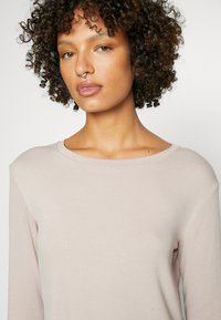 Helle beige gerippte Langarmbluse mit weitem Ausschnitt und weichem Stoff. Enganliegende Ärmel und dezente Nähdetails an den Nähten.